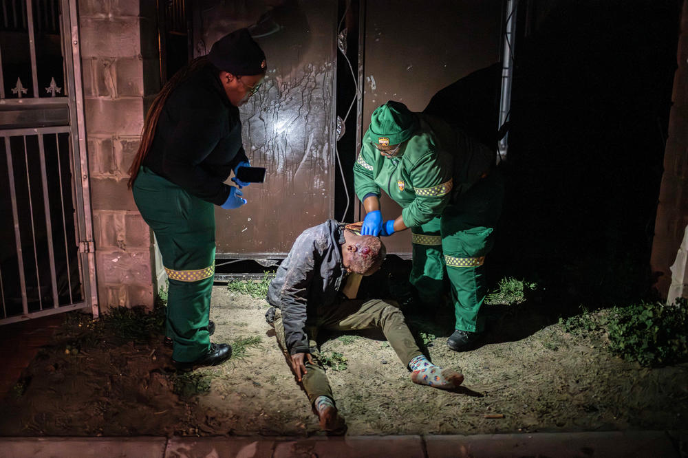 Paramedics Yozi Thomza and Yandiswa Mtshelma attend to a man who was stabbed 13 times in the back and head by robbers who wanted his shoes and mobile phone. The attack took place in a gang-afflicted neighborhood in the Cape Flats, Cape Town.
