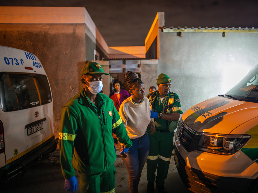 Paramedics Zuko Faltein (left) and Papinki Lebelo (right) help a patient to an ambulance in a designated Red Zone neighborhood in Cape Town.