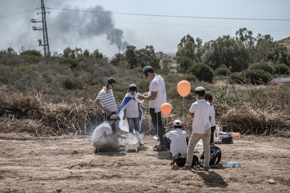 Israeli settlers at a barbecue as smoke rises from Gaza Strip during Israel's Independence Day, May 14.