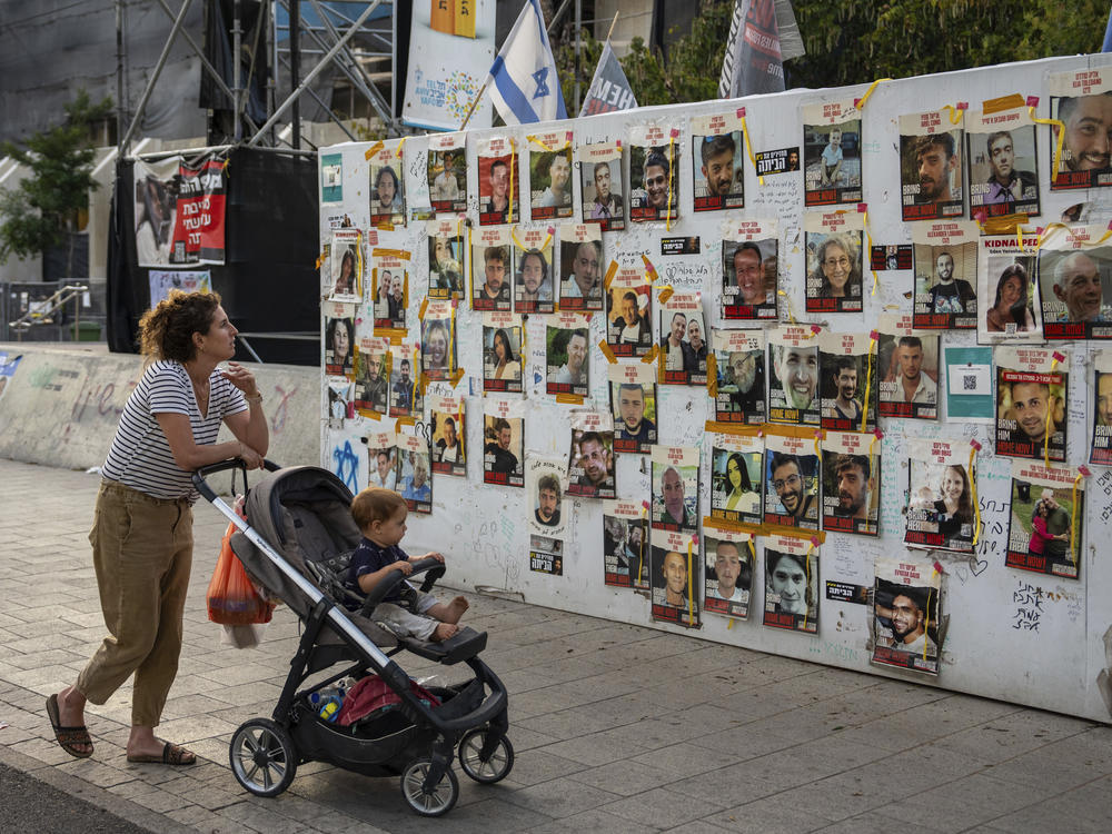 Passersby observe the photos of hostages held in the Gaza Strip that are plastered to the walls of a plaza known as Hostages Square in Tel Aviv, Israel, Friday, May 17, 2024.