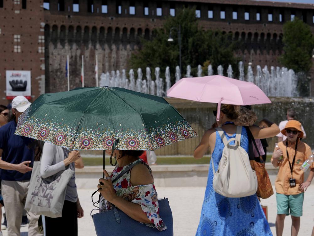 Tourists shelter from the sun in front of the Sforzesco Castle in Milan, Italy, on Tuesday. Weather alerts, forest fires, melting pavement in cities: A sizzling heat wave has sent temperatures in parts of central and southern Europe soaring toward 104 degrees Fahrenheit (40 degrees Celsius) in some places.