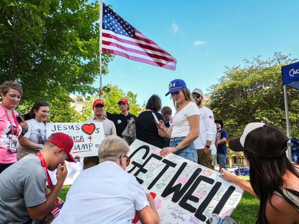 A group gathers to write on a poster board set out for well wishes for Donald Trump toward the end of the Prayer Vigil for America held at Zeidler Union Square in Milwaukee on Sunday.