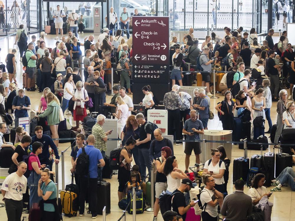 Passengers wait in front of check-in counters at the capital's Berlin Brandenburg Airport, in Schönefeld, Germany, on Friday after a widespread technology outage disrupted flights, banks, media outlets and companies around the world.