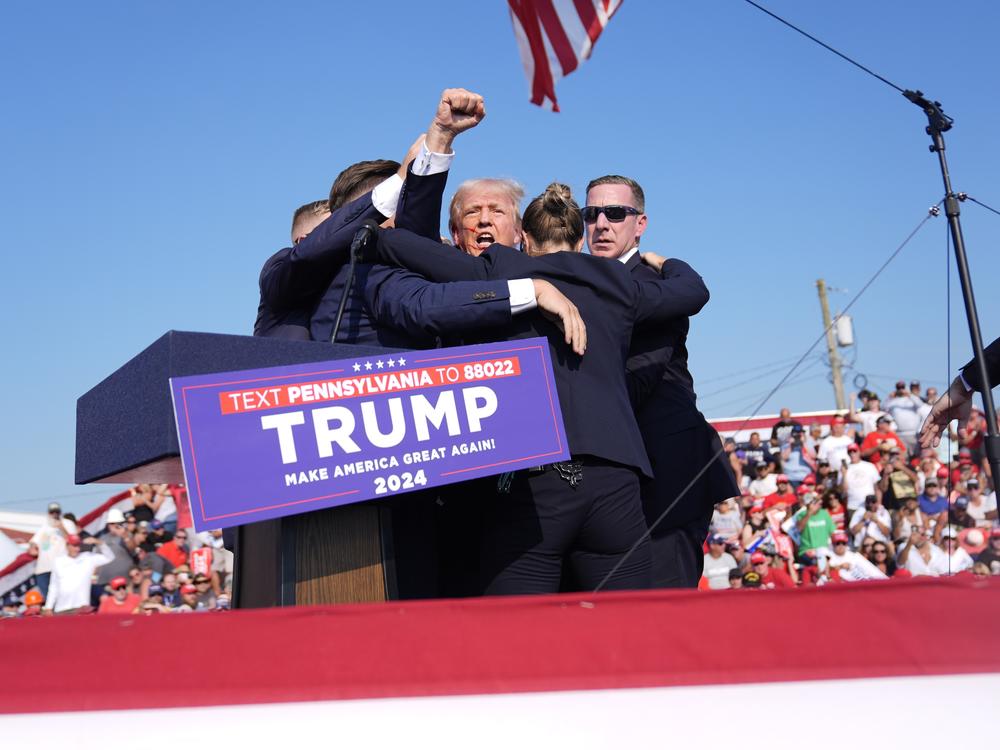 Trump holds a fist in the air as Secret Service agents surround him as he is rushed offstage at the campaign rally in Butler on July 13.