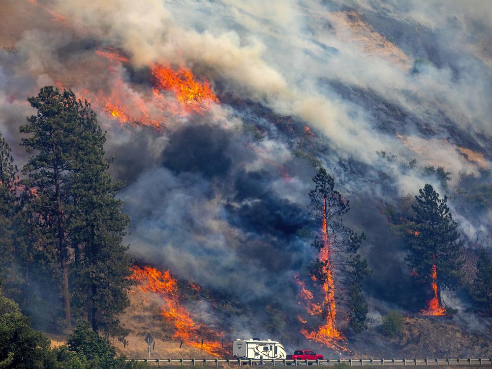 A vehicle drives past the spreading River Fire Thursday, July 25, 2024, near Myrtle, Idaho, before U.S. Highway 12 was closed. Lightning strikes have sparked fast-moving wildfires in Idaho, prompting the evacuation of multiple communities.