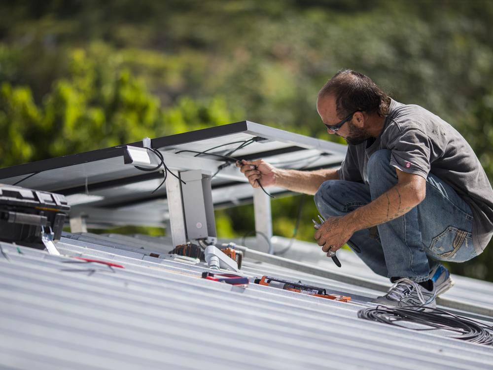 A technician installs a solar energy system at a home in 2018, in Adjuntas, Puerto Rico. Across the U.S. solar power is booming and that helps the country meet its climate goals by replacing fossil fuels. 