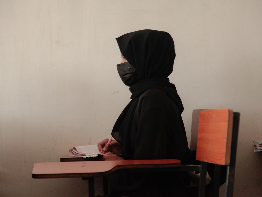 A teenage girl wearing a face mask, head scarf and long black robe, listens to a math teacher at a tutoring center in Kabul. The center was established by a women's rights activist to circumvent a Taliban ban on girls attending secondary school. The activist said she has informal permission by Taliban authorities to run the center as long as teenage girls abide by a strict dress code.