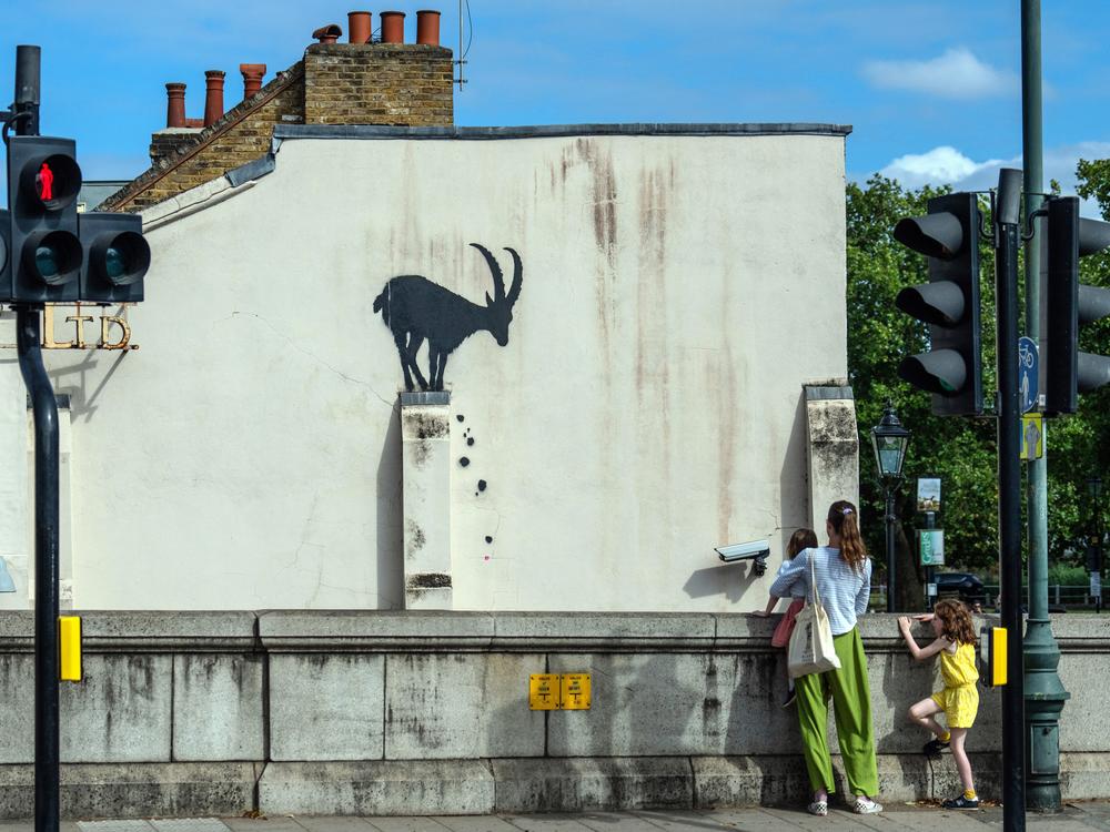 A woman and children view a mural depicting a goat by the street artist Bansky, on Aug. 5.