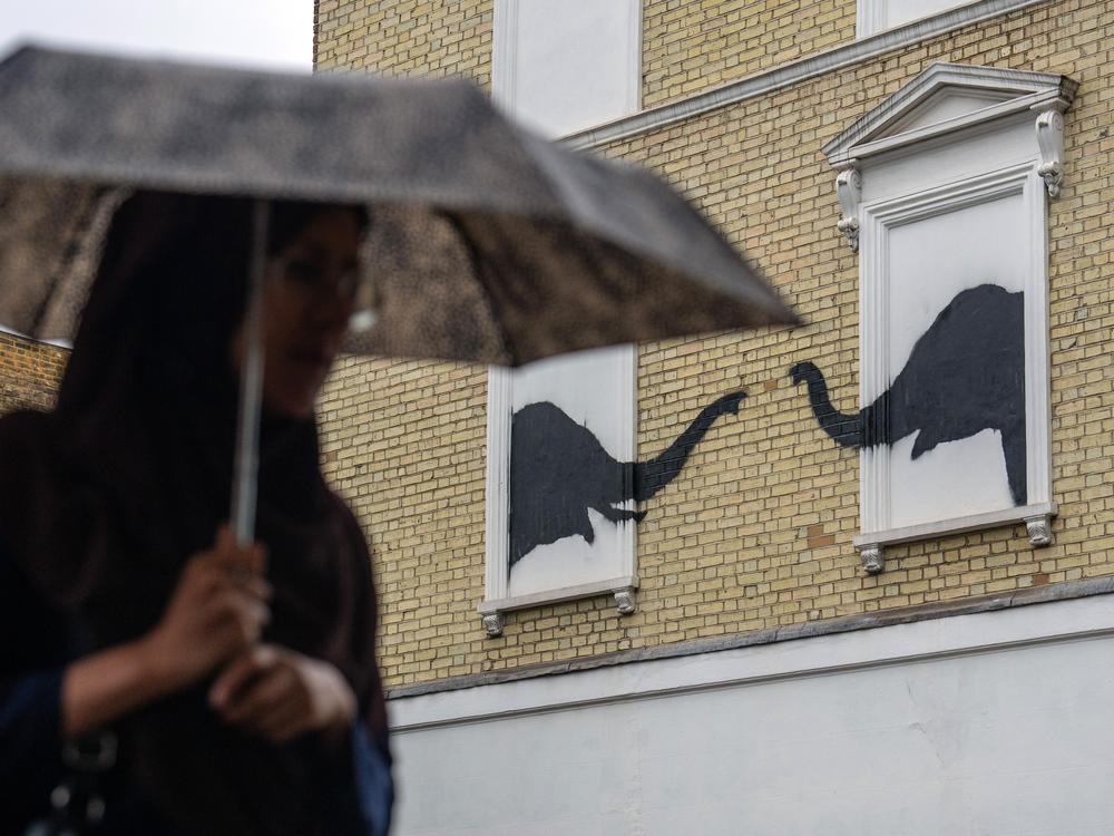 A woman walks past an artwork featuring two elephants, purportedly by Banksy, on a residential building on Aug. 6.