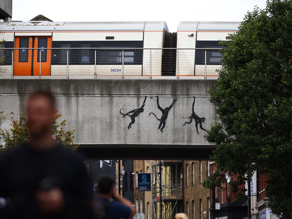 A train goes past an artwork by street artist Banksy, depicting three monkeys, painted on the side of a railway bridge in east London on Aug. 7.