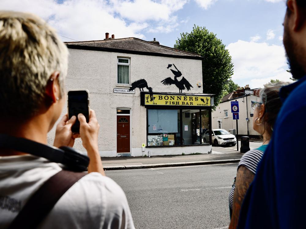 People gather to look at an artwork by street artist Banksy depicting two pelicans catching fish, painted on top of a fish-and-chips shop in Walthamstow, northeast London, on Aug. 9.