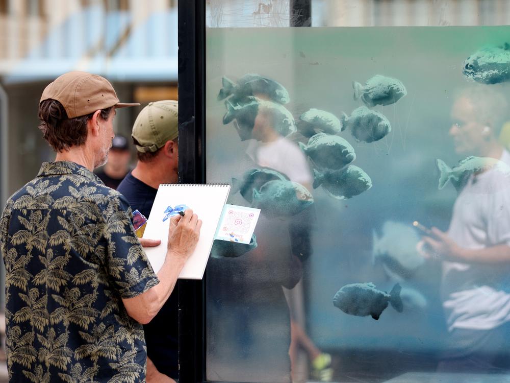 A person draws artwork in front of one of the recent pieces by Banksy, in which fish adorn a a London Police box on Ludgate Hill, on Aug. 11.