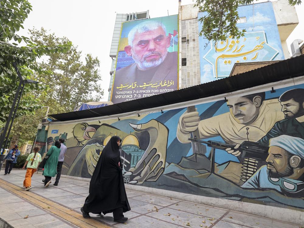 People walk past a billboard showing a portrait of Hamas leader Yahya Sinwar (top) next to Palestine Square in the Tehran on Aug. 12, 2024.