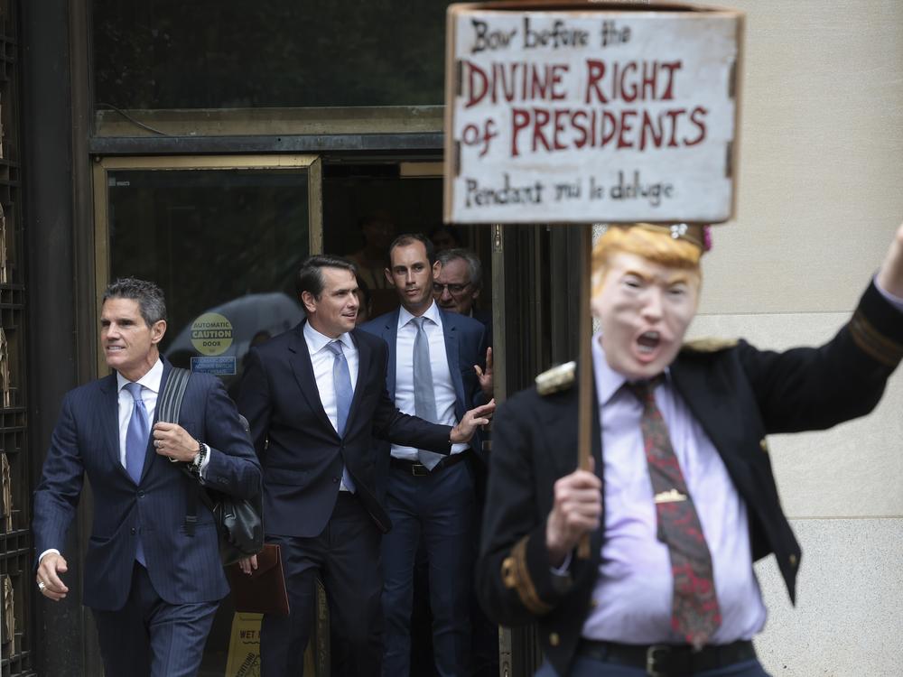 Attorneys for former President Donald Trump, John Lauro (left) and Todd Blanche (second left), depart the E. Barrett Prettyman U.S. Courthouse in Washington, D.C., in 2023, near a protester wearing a costume in Trump's likeness.