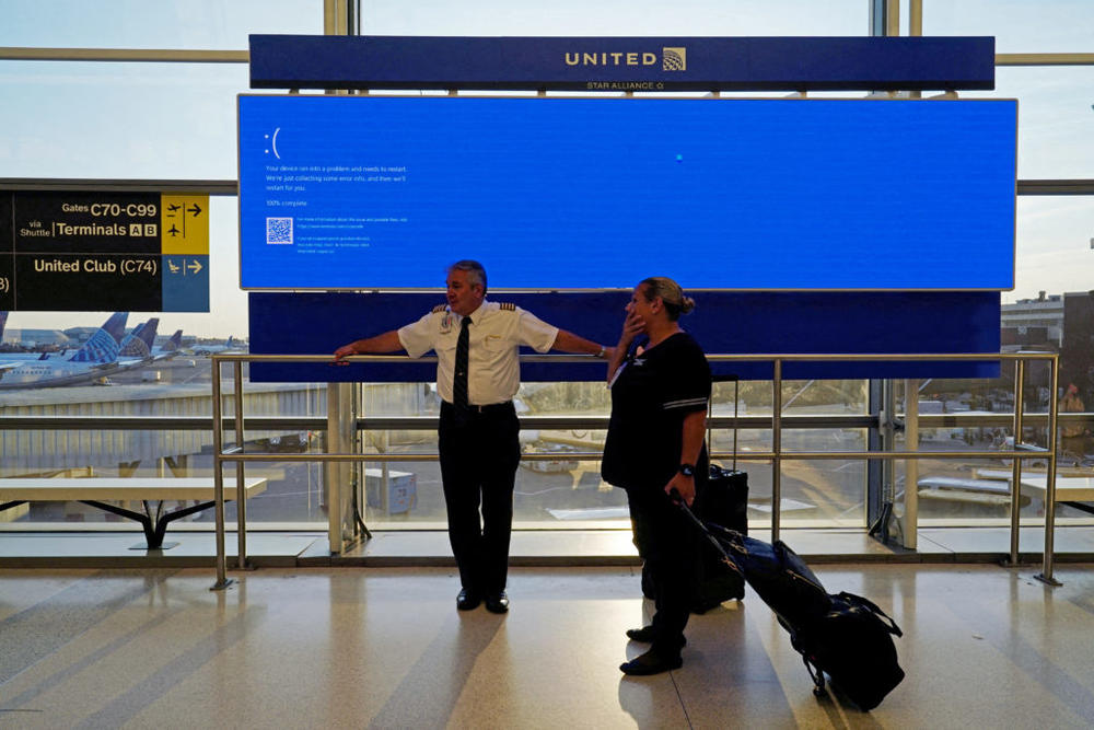 United Airlines employees wait by a departures monitor displaying a blue error screen, also known as the "Blue Screen of Death" inside Terminal C in Newark International Airport, after United Airlines and other airlines grounded flights due to a worldwide tech outage caused by an update to CrowdStrike's "Falcon Sensor" software in Newark, New Jersey, on July 19, 2024. Photo by Bing Guan/ Reuters