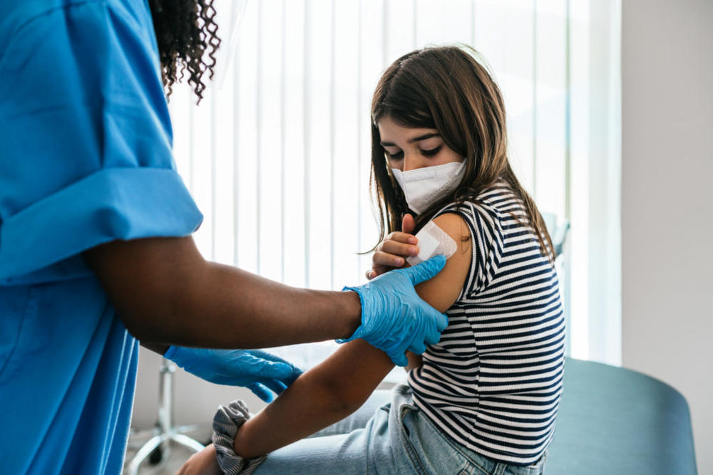 Unrecognizable female doctor or nurse putting a bandage after Covid-19 vaccination at vaccination center. Caucasian preteen girl in vaccination center.