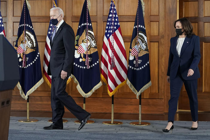 President Joe Biden and Kamala Harris walk together on a stage by American flags.