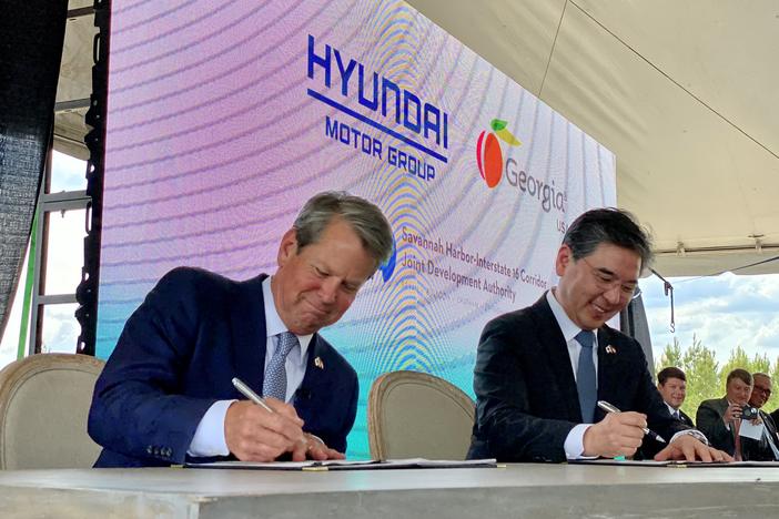 Georgia Governor Brian Kemp and Hyundai Motor Group president and CEO JaeHoon Chang are seated at a table and smiling as they each sign papers.