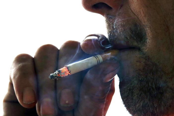 A closeup of a person's nose, mouth and hand while smoking a cigarette