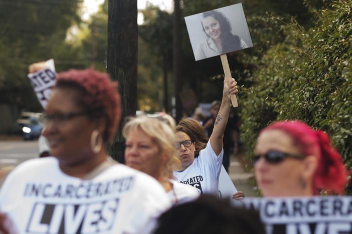 A protester carries a photo of Stephanie Widener who died of sepsis in Georgia Department of Corrections custody during a protest of prison conditions outside the Georgia Governor's Mansion on October 3, 2023.