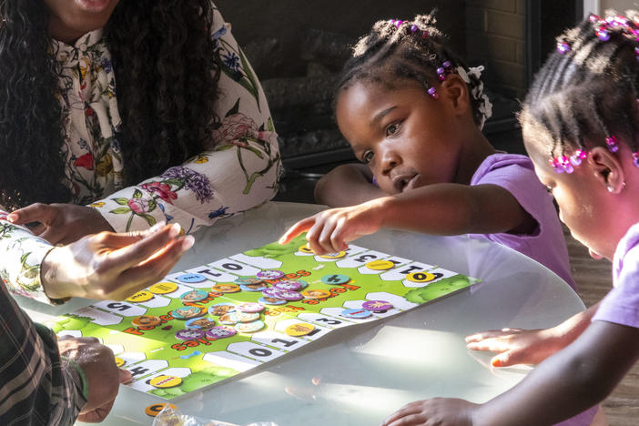 Justice, center, points to a number on the board game in front of her.