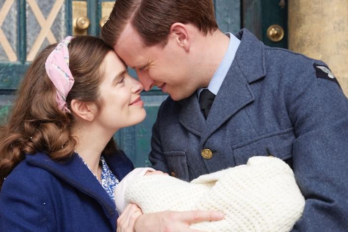 A young couple embrace with their infant in a doorway.