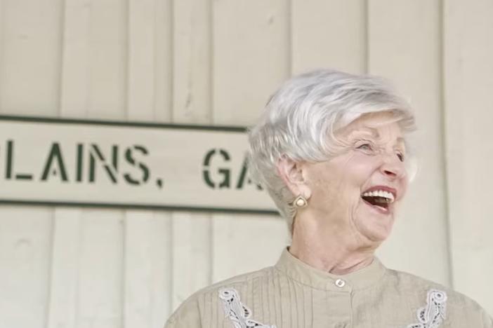 An elderly woman standing on a train platform.