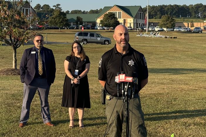 Barrow County Sheriff Jud Smith and two other people are shown standing on the grass lawn in front of Apalachee High School.