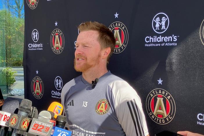 Dax McCarty is shown in an Atlanta United uniform speaking behind a podium.