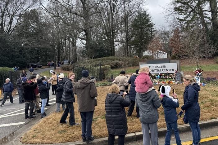 After paying respects to former President Jimmy Carter, mourners visit the entrance sign to the Carter Presidential Center as they make their way out of the property on Mon. Jan. 6, 2024.