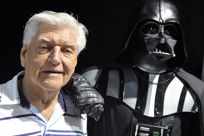 British actor David Prowse, who played Darth Vader in the first Star Wars trilogy, poses with a fan dressed in a Darth Vader costume during a Star Wars convention on April 27, 2013. On Sunday morning, Prowse's management company shared the news of his death at age 85.