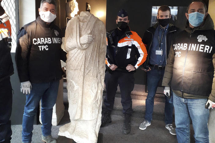 Carabinieri (Italian paramilitary police) officers of the art squad's archaeological unit pose with a headless Roman statue wearing a draped toga in Brussels on Wednesday, Feb. 3, 2021.