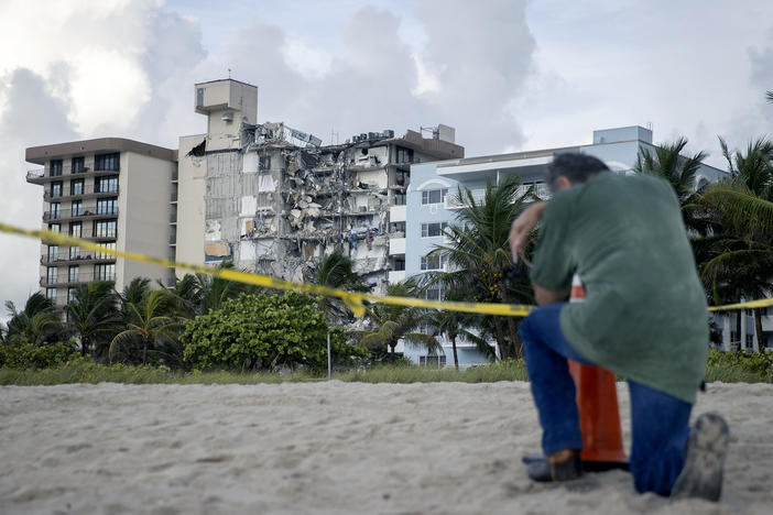 A man prays Friday near where search and rescue operations are ongoing at the partially collapsed 12-story Champlain Towers South condo building in Surfside, Fla.