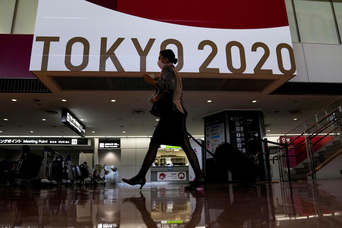 A flight attendant walks by a large display of Tokyo 2020 Olympics at Narita International Airport on Thursday in Narita, east of Tokyo.