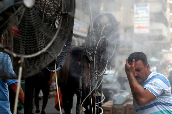 A man stands by fans spraying air mixed with water vapor deployed by donors to cool down pedestrians along a street in Iraq's capital Baghdad on June 30 amid a severe heat wave.