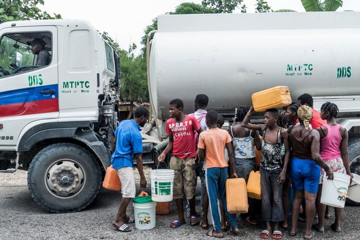 People gather near bins of water in Camp-Perrin, Haiti, on Monday.