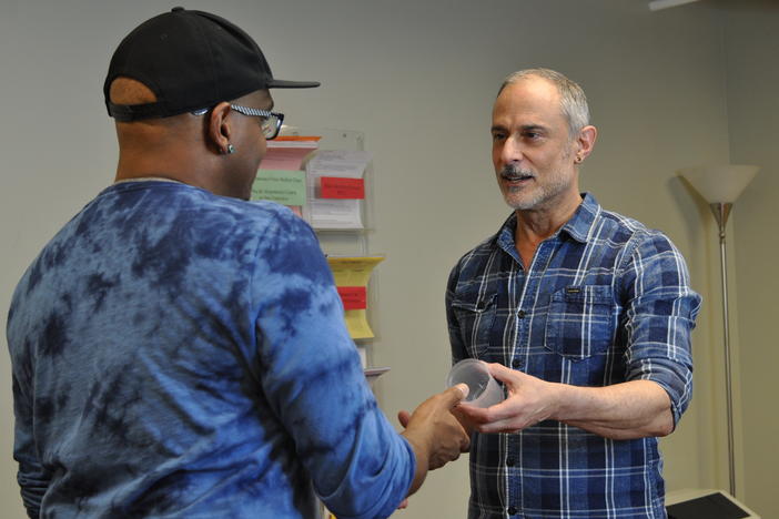 At the San Francisco AIDS Foundation, staff members Tyrone Clifford (left) and Rick Andrews (right) demonstrate how a contingency management visit typically begins, with a participant picking up a specimen cup for a urine sample. If the sample tests negative for meth or cocaine use, the participant has an incentive dollar amount added to their "bank" which can later be traded for a gift card.