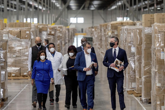 Gov. Gavin Newsom, right, walks through rows of boxed personal protective equipment with dignitaries and elected officials, as he prepares to announce the next phase of California's COVID-19 response on Thursday.