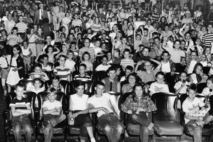 An audience of mostly children cheer and make faces in a movie theater, mid 1950s.