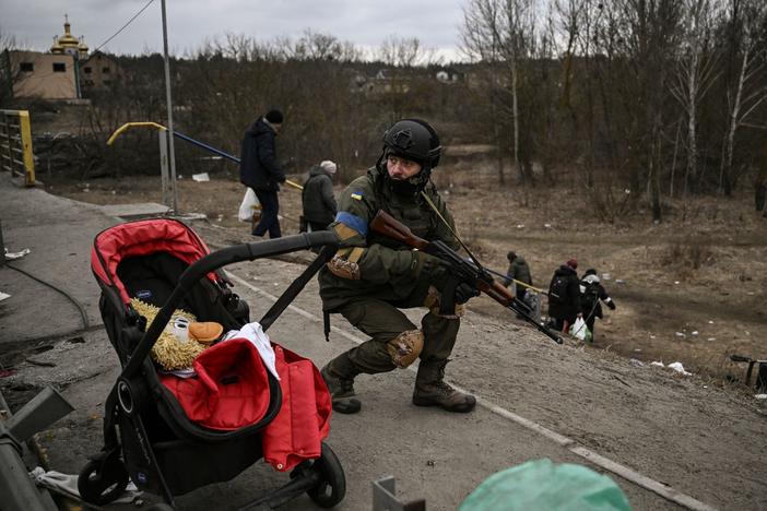 A Ukrainian serviceman takes cover as people evacuate the city of Irpin, near Kyiv, on Sunday.