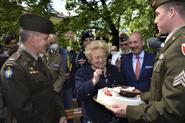 Soldiers from U.S. Army Garrison Italy return a birthday cake to Meri Mion, center, in Vicenza, northern Italy, Thursday, April 28, 2022, to replace the one U.S. soldiers ate as they entered her hometown during one of the final battles of World War II. Mion, who turns 90 on Friday, wiped away tears as she was presented with the cake.