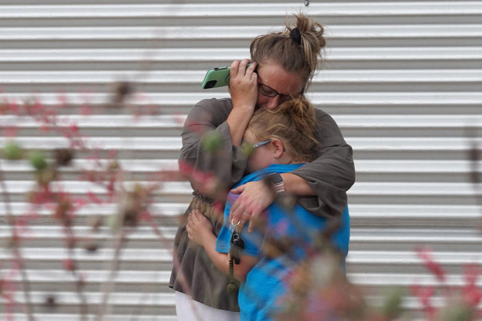 A woman cries and hugs a young girl while on the phone outside the Willie de Leon Civic Center where grief counseling will be offered in Uvalde, Texas.