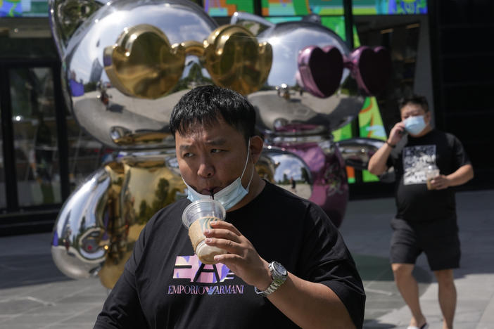 A man lowers his mask to drink from a cup as he past near a mall, Wednesday, July 13, 2022, in Beijing.