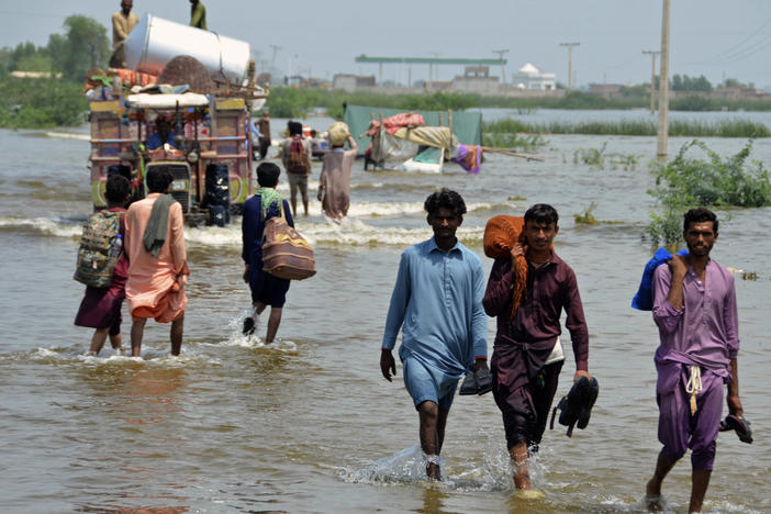 People wade through a flooded area in Pakistan, that has been dealing with what people are calling "monster monsoons".