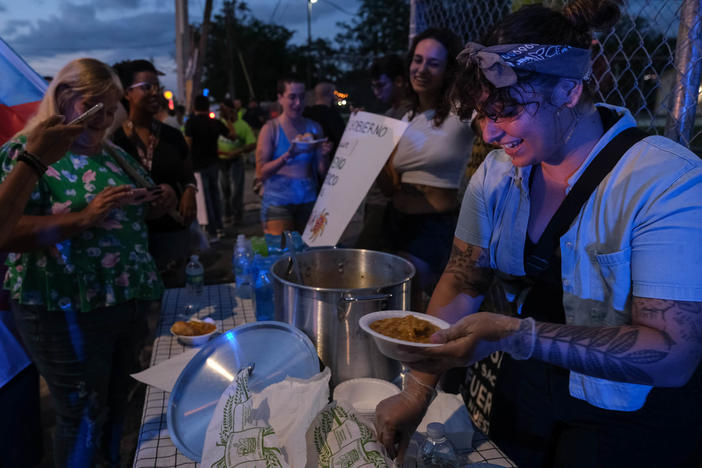 Lorraine Arroyo RomÃ¡n serves "asopao" during a protest against LUMA Energy in Aguadilla, Puerto Rico on Saturday. RomÃ¡n is illuminated by the lights of police vehicles.