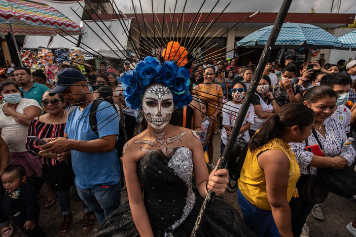 Una joven vestida con maquillaje de Santa Muerte espera afuera del panteón con algunos participantes