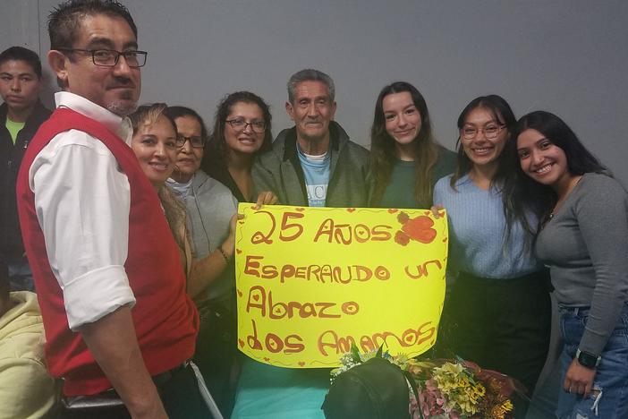 The Rodriguez Tellez family poses for a picture, together for the first time in 25 years. The sign says, "25 years waiting for a hug. We love you."