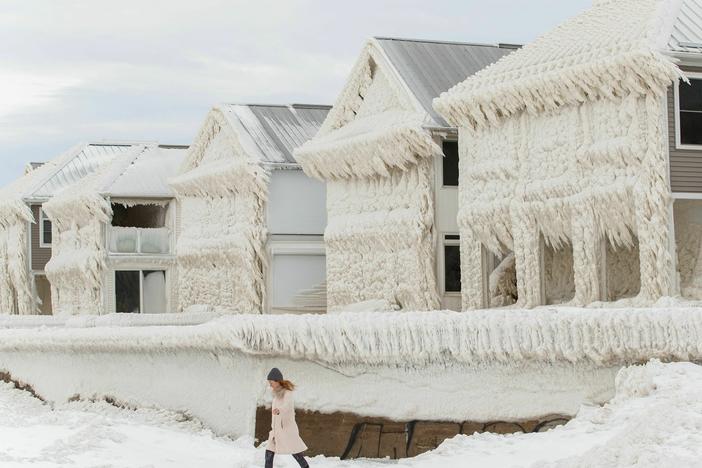 A person walks by homes covered in ice at the waterfront community of Crystal Beach in Fort Erie, Ontario, Canada, on Wednesday, following a massive snowstorm that knocked out power in the area to thousands of residents.