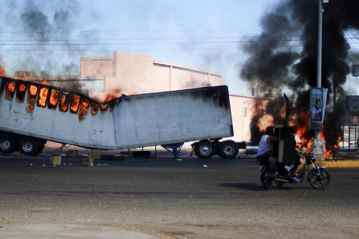 Men ride on a motorcycle past a burning truck on the streets of Culiacan, Sinaloa state, Thursday, Jan. 5, 2023. Mexican security forces have captured Ovidio Guzmán, an alleged drug trafficker wanted by the United States and one of the sons of former Sinaloa cartel boss Joaquín "El Chapo" Guzmán.