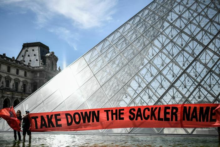 Activists hold a banner reading "Take down the Sackler name" in front of the Pyramid of the Louvre museum in Paris on July 1, 2019.